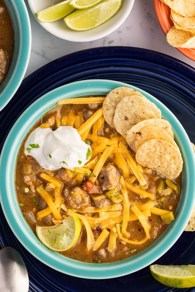 Bowl of Colorado-style pork green chili served with cheese, sour cream, chips and lime.