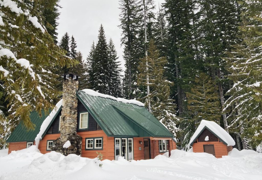 Cabin in the woods half buried in snow.