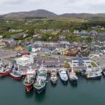 A busy fishing port with fishing vessels docked, industry equipment, and surrounding hills.