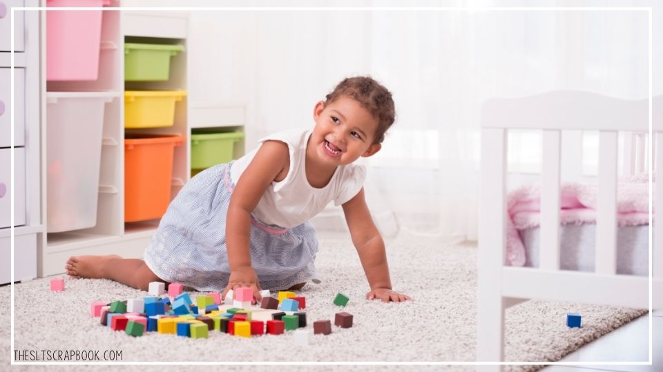 Picture of a young girl playing with blocks in her bedroom. Toy storage for effective toy rotation can be seen in the background