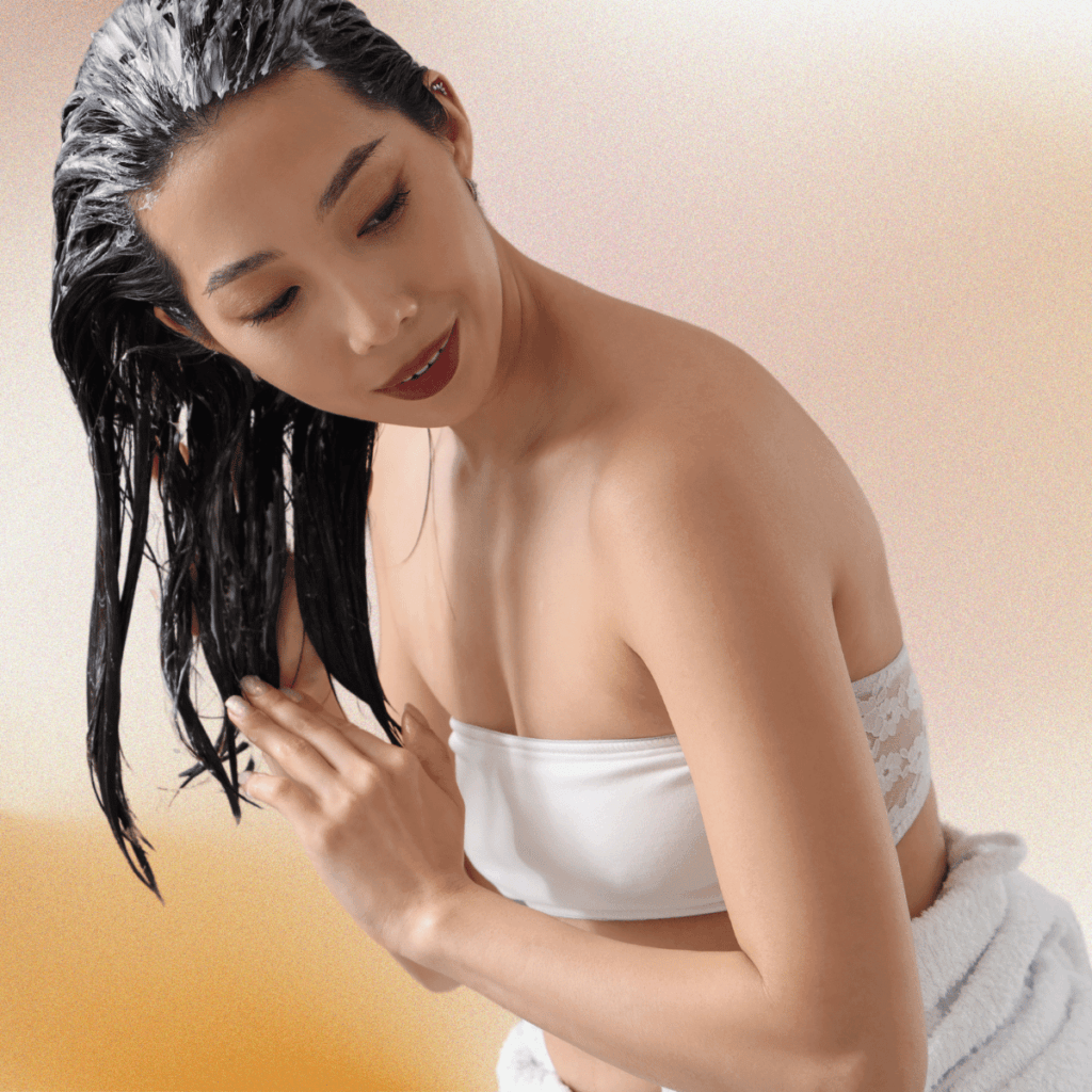 Woman applying a hair mask to her hair on gradient brown background