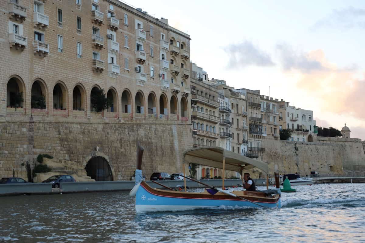 Picturesque Maltese coastal town with historic buildings and boat on the water.