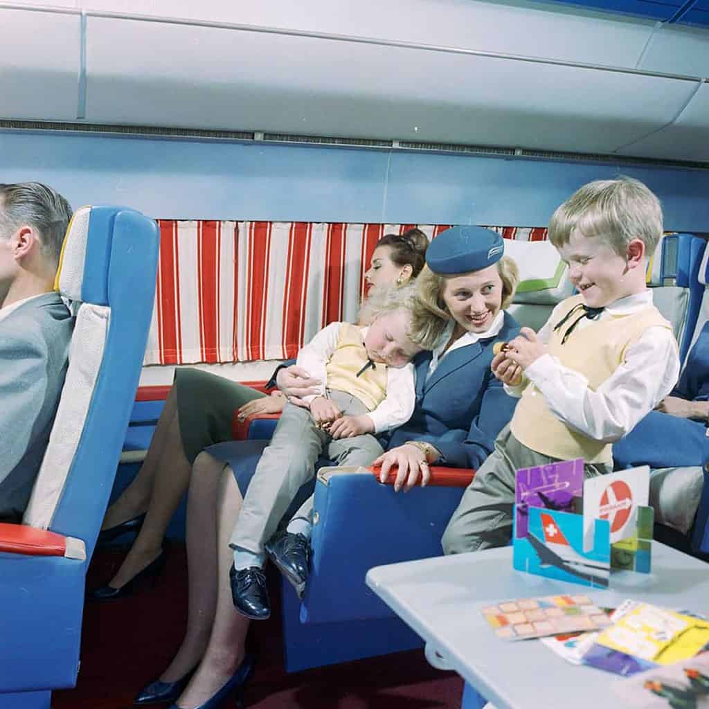 Flight attendant taking care of a sleeping child in 1960 First Class