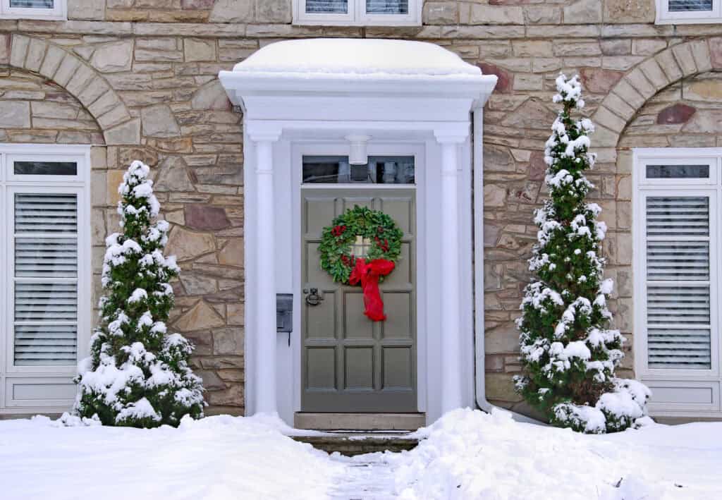 Christmas front door with holiday wreath, snow-covered decorations, and stone house exterior, showcasing professional residential painting services.