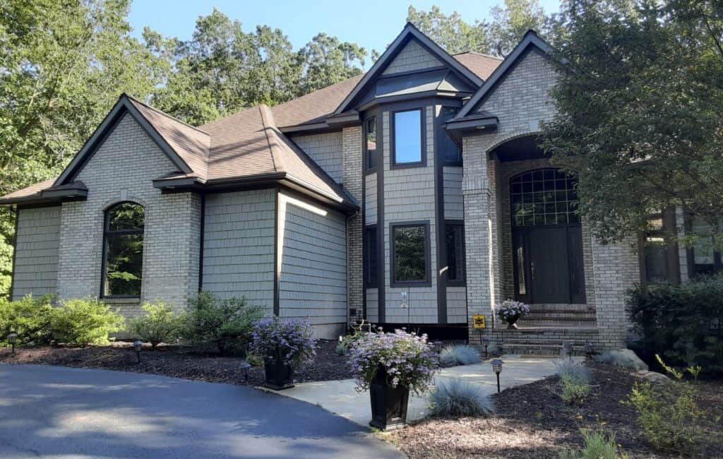 Elegant custom home exterior featuring a blend of brick and siding, surrounded by lush landscaping; expert painting services enhance the California-style architecture.