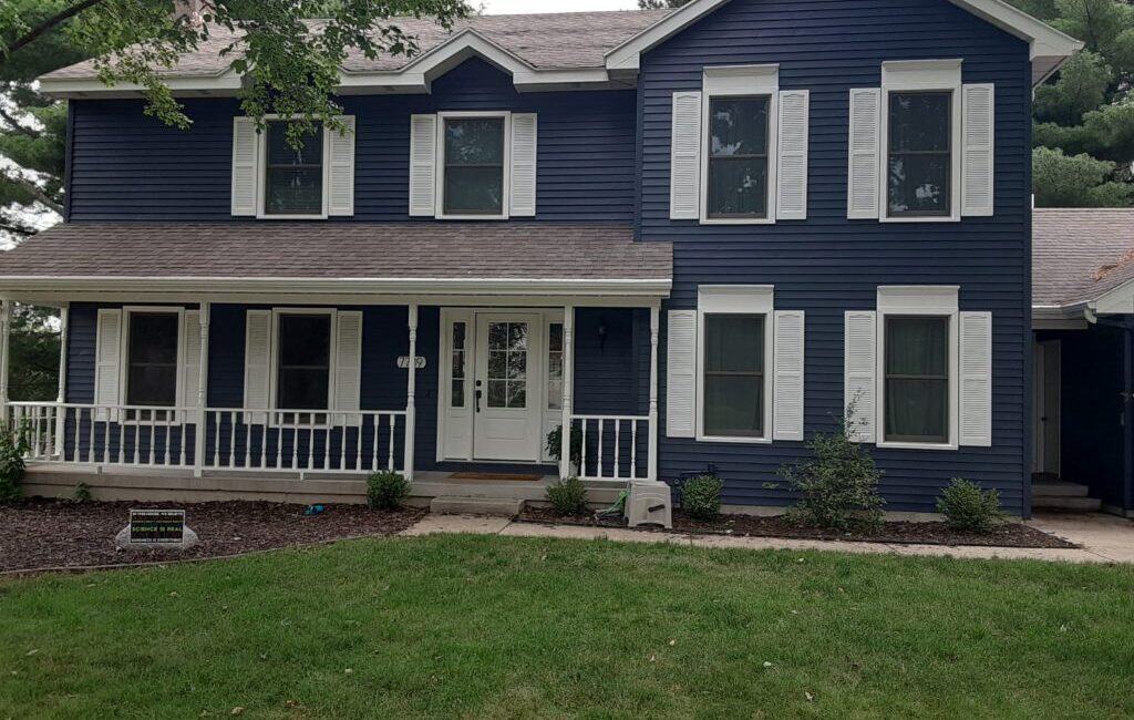 Bright blue exterior house with white trim and shutters, featuring a front porch, well-maintained lawn, and landscaping, showcasing professional exterior house painting services.