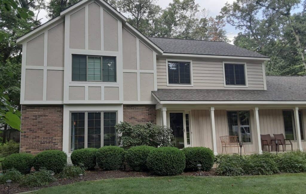 Modern suburban house with mixed brick and siding exterior, surrounded by lush landscaping and mature trees, showcasing professional exterior painting and home improvement services.