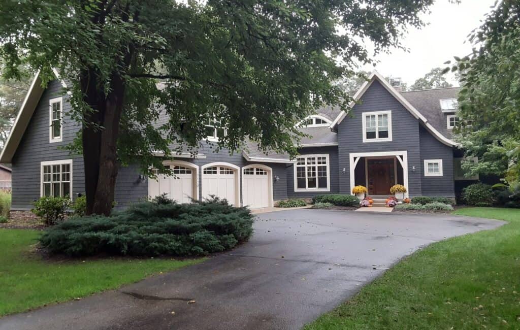 Bright blue exterior house with white accents, surrounded by lush greenery and trees, showcasing professional Thornapple Painting work on residential property.