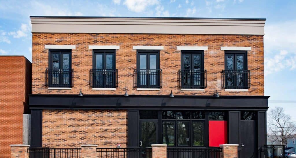 Modern brick commercial building with black accents and red door, featuring three floors and balcony railings, ideal for business or retail spaces.