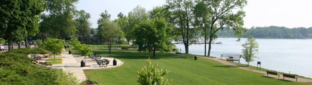 Lush green park with walking paths, benches, trees, and a lakeside view, offering a tranquil outdoor setting for relaxation and recreation.