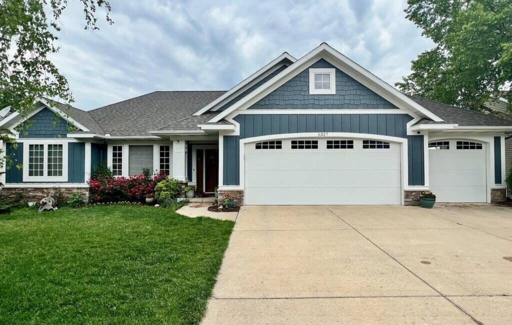 Neat blue and white residential house with fresh siding and landscaped front yard, excellent exterior painting and home improvement by Thornapple Painting.