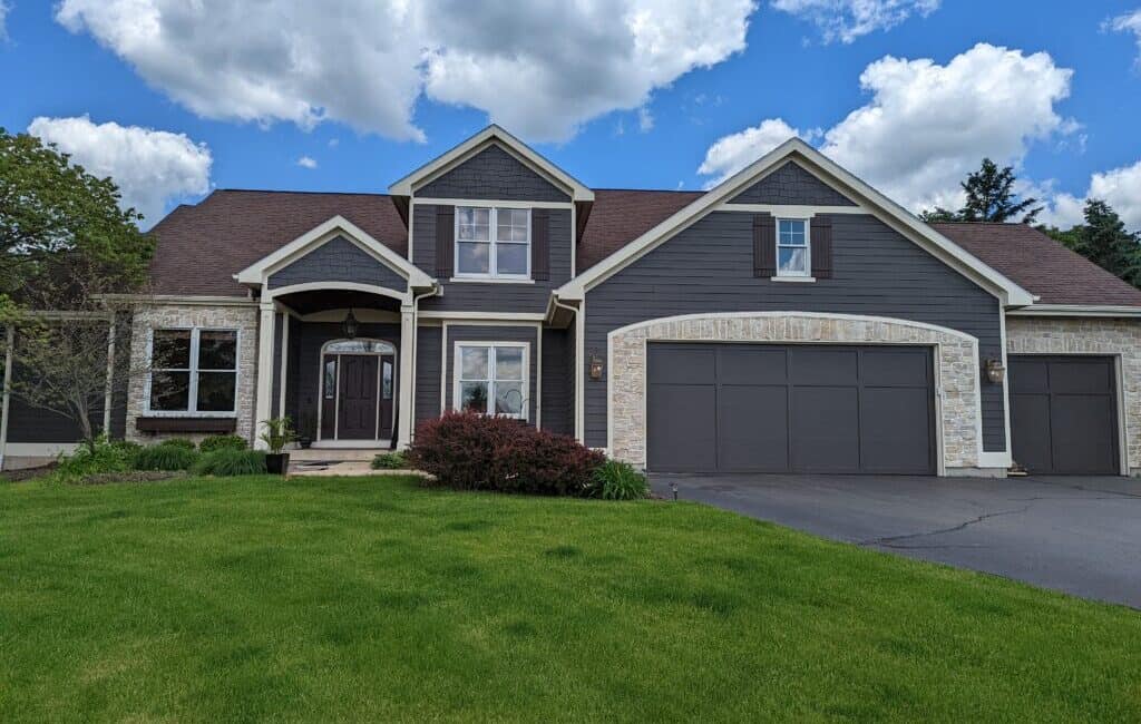Modern house exterior painted with dark gray siding and white stone accents, featuring a new garage door and landscaped front yard with lush green grass.