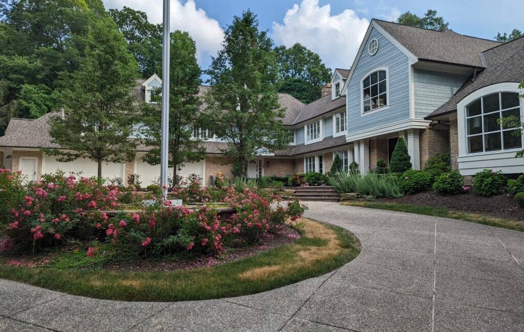 Modern residential house with landscaped garden and driveway in a suburban neighborhood, featuring lush greenery and beautiful flowering plants.