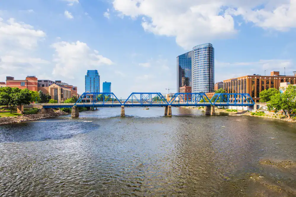 Vibrant cityscape of Grand Rapids featuring the Thornapple River, modern high-rise buildings, and a distinctive blue bridge emphasized in professional exterior painting.