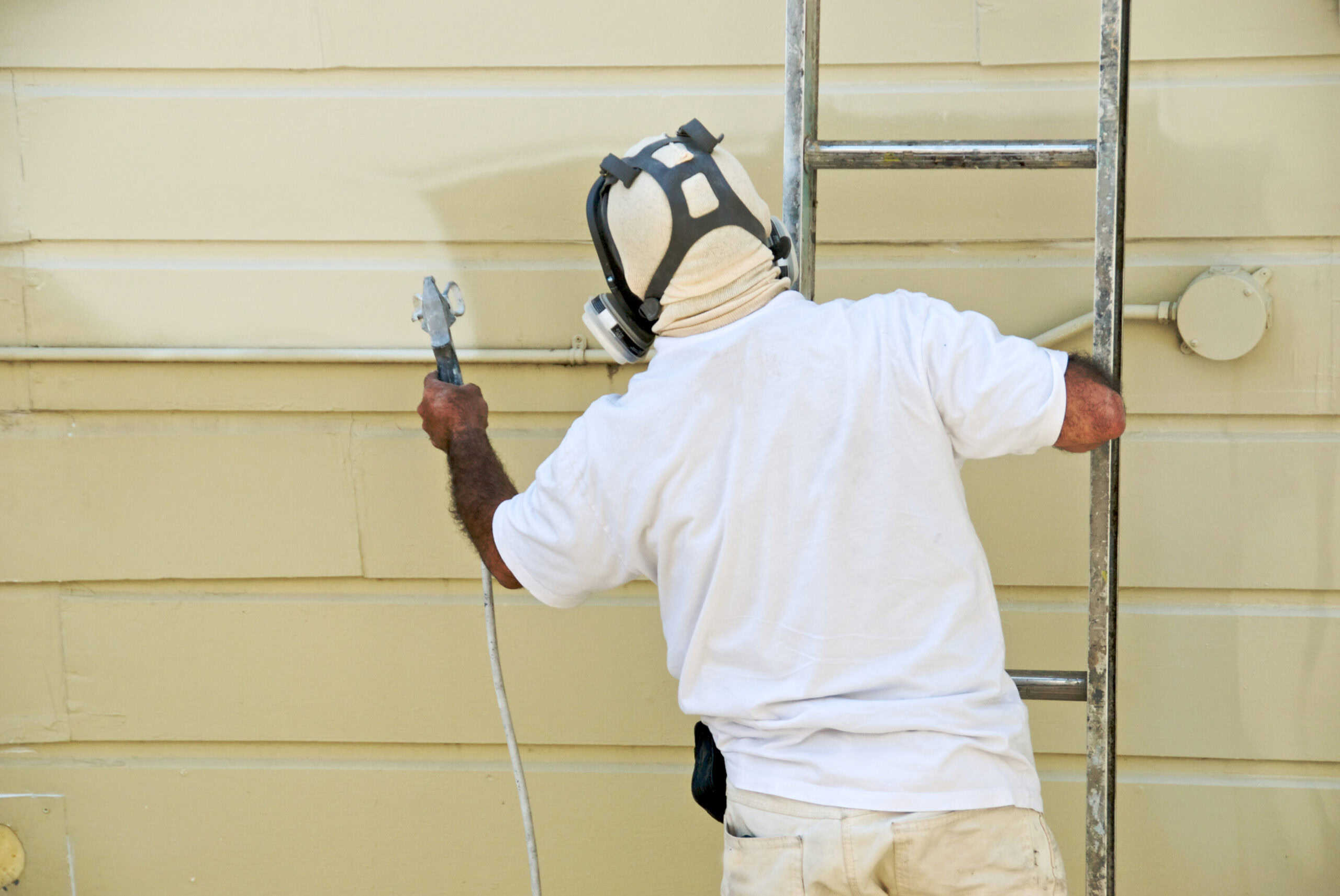 High-quality house painter working on exterior siding with scaffolding, showcasing professional painting services for residential homes, ensuring a smooth and durable finish.