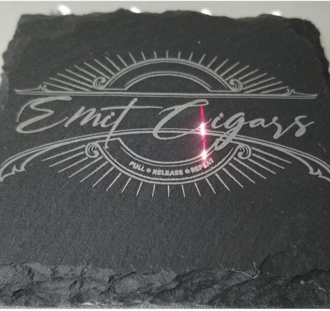 Intricately engraved cigar band on black slate, customized for smoking accessories with elegant design.