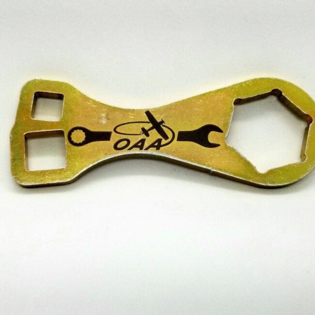 Vintage metal bottle opener with custom engraving, featuring tools and the text "OAA.".