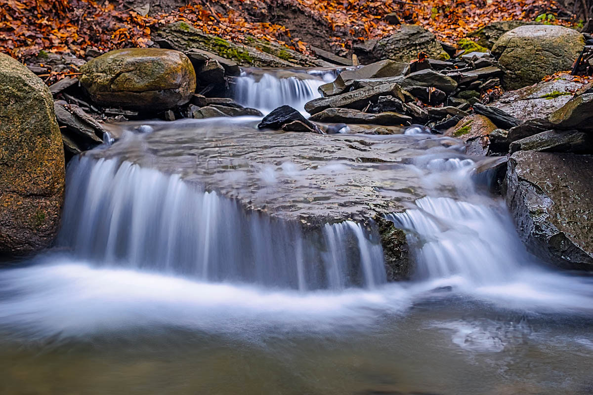 Water flowing and falling over a large triangular rock in a small stream.