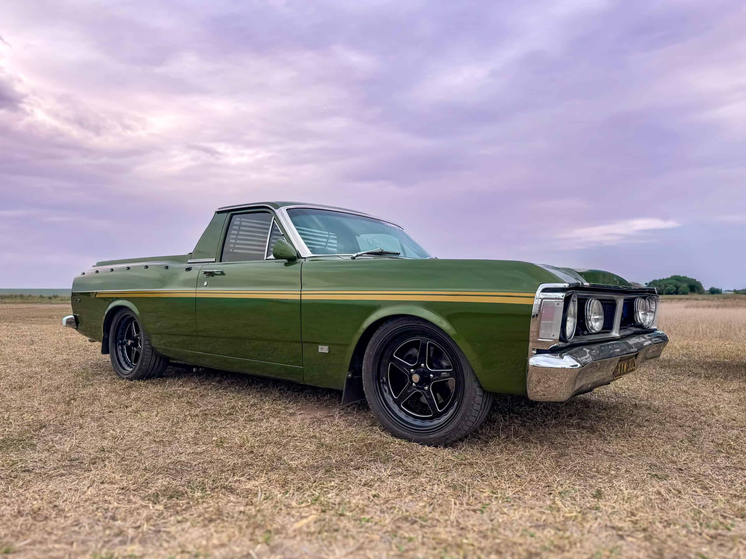 Vintage green pickup truck parked on open field under cloudy sky.