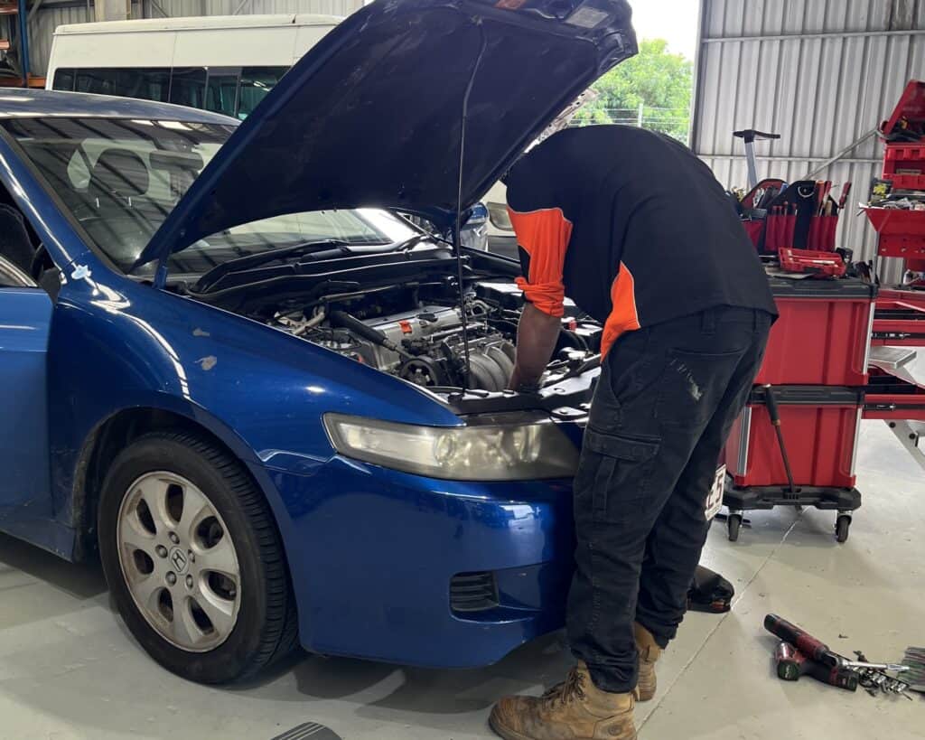 Auto electrical technician working on a blue car engine.