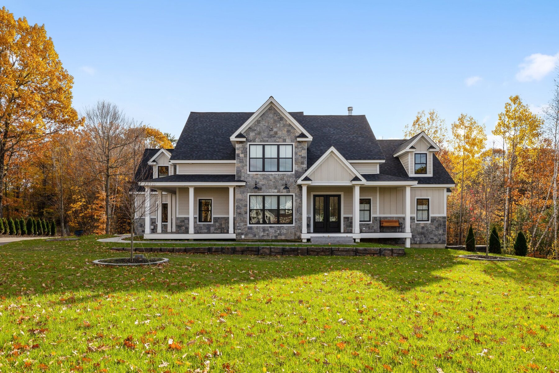 Large two-story house with stone and light siding, surrounded by autumn trees.