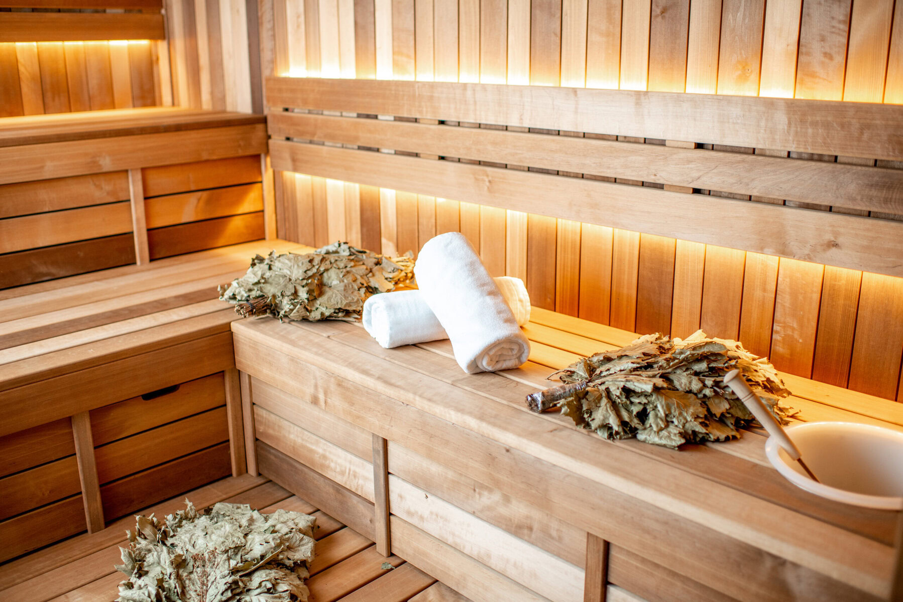 Interior of a wooden sauna with towels, dried leaves, and a bucket
