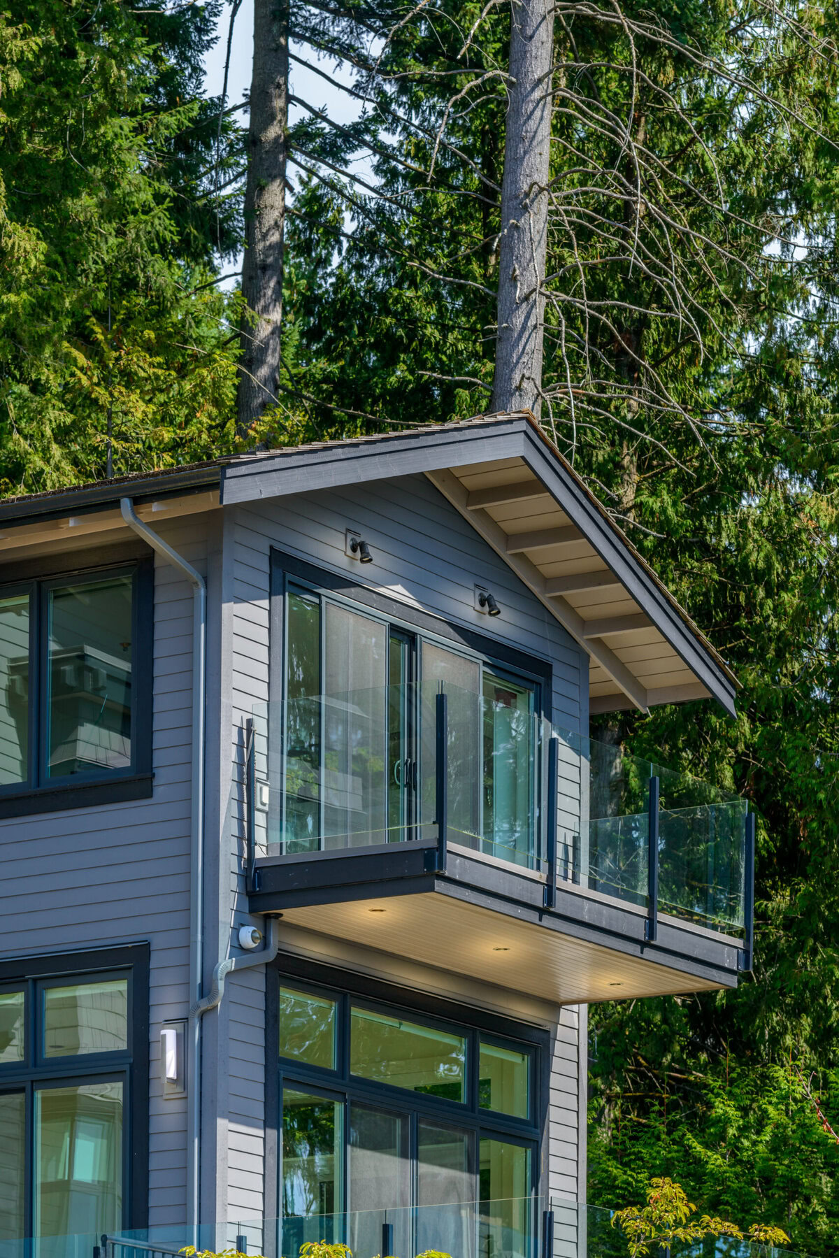 Modern house exterior with balcony and large windows surrounded by trees.