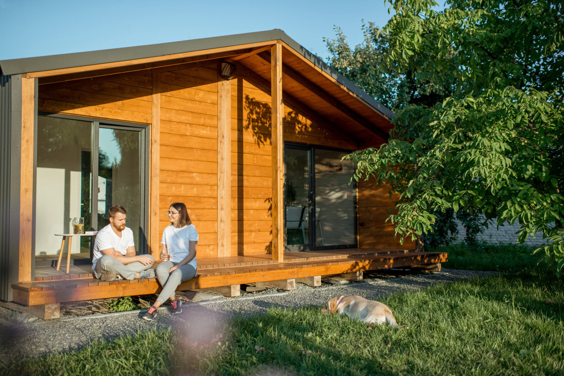 Couple and dog relaxing outside a modern wooden house on a sunny day
