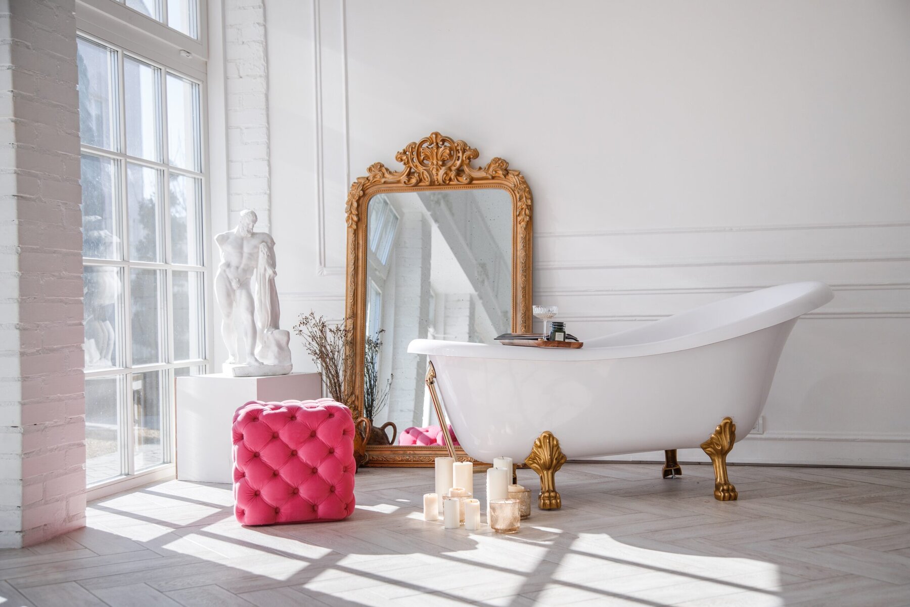 White bathroom with clawfoot tub, ornate mirror, and pink ottoman