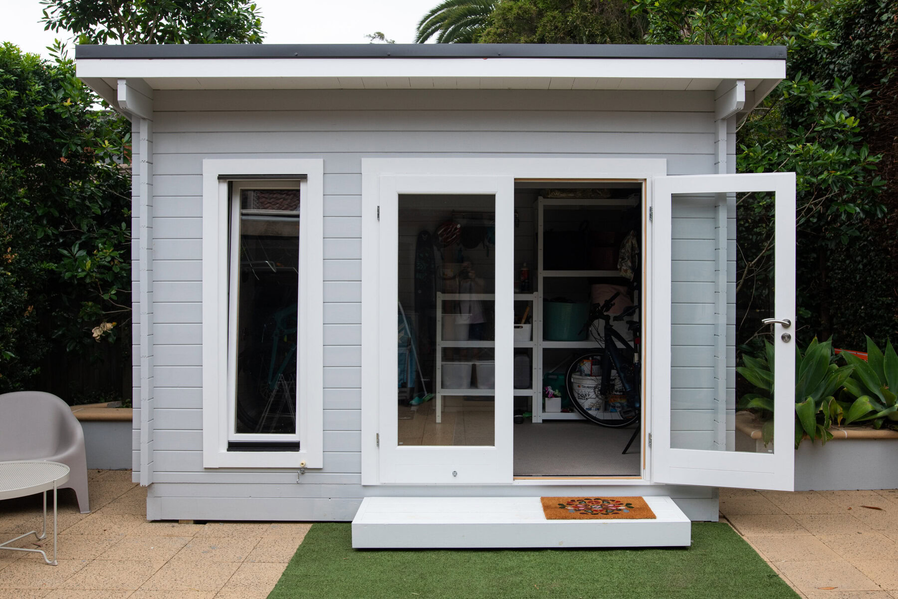 Light grey shed with white trim, open double doors, and a single window.