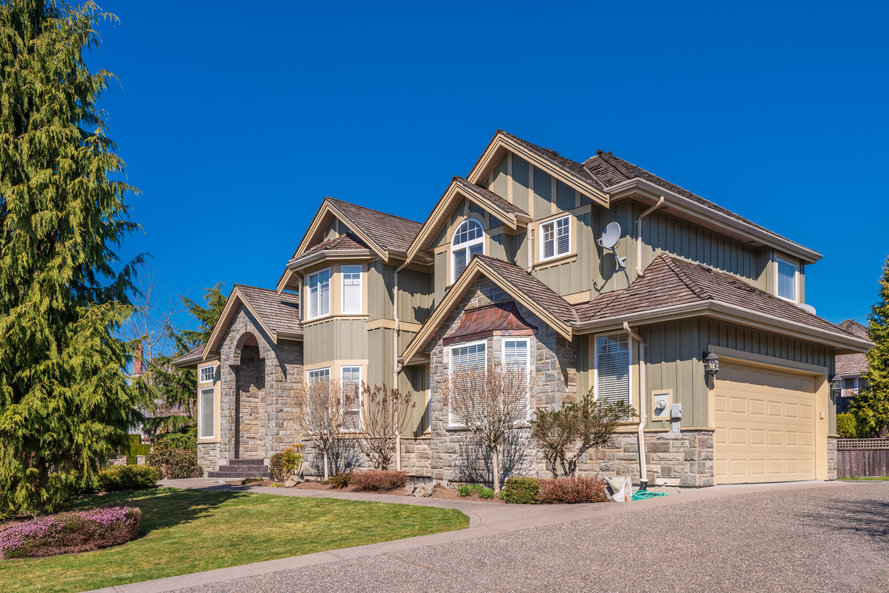 Large two-story house with stone and siding exterior under a clear blue sky.