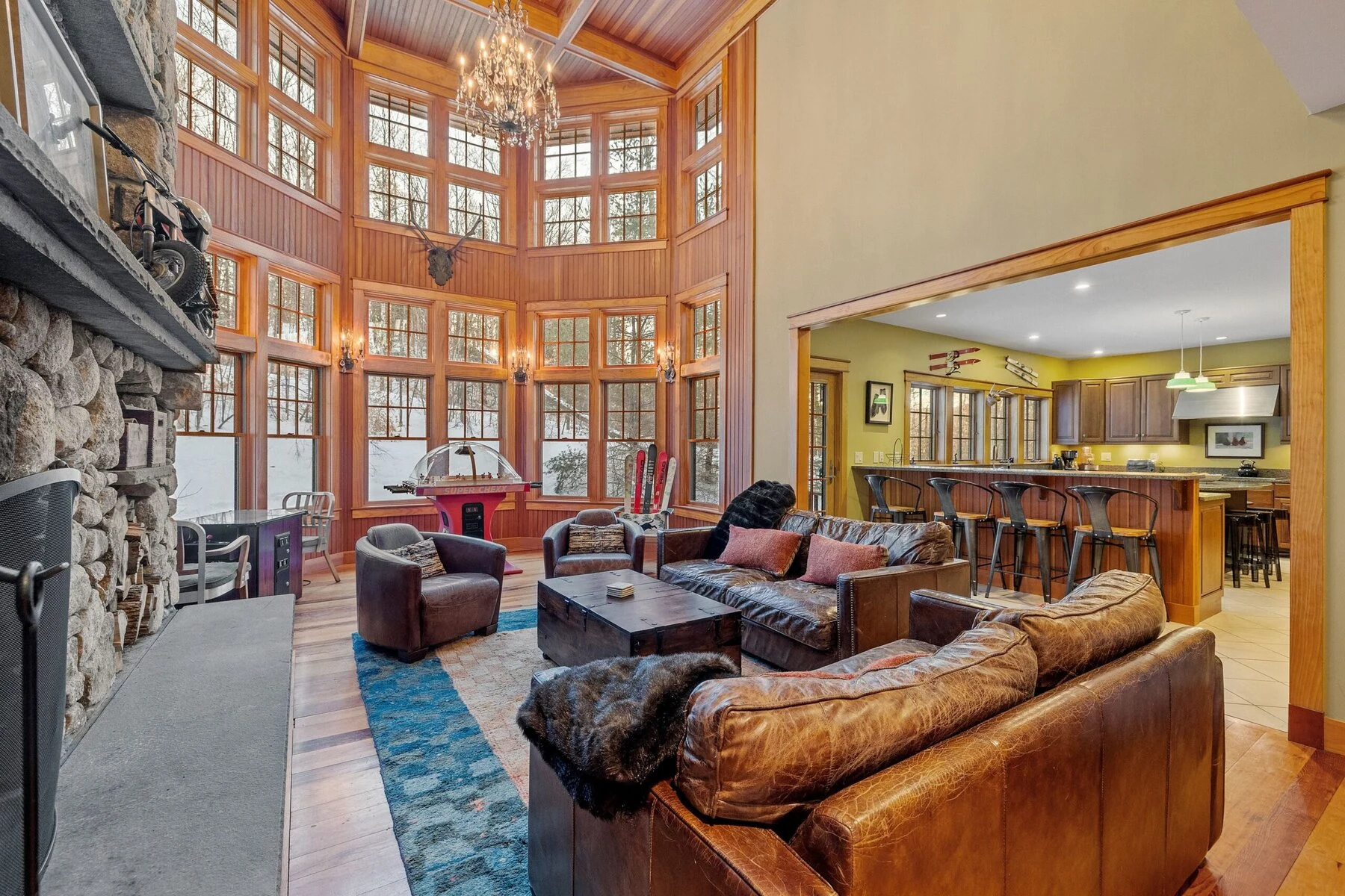 A spacious living room with large windows, leather sofas, and a stone fireplace.