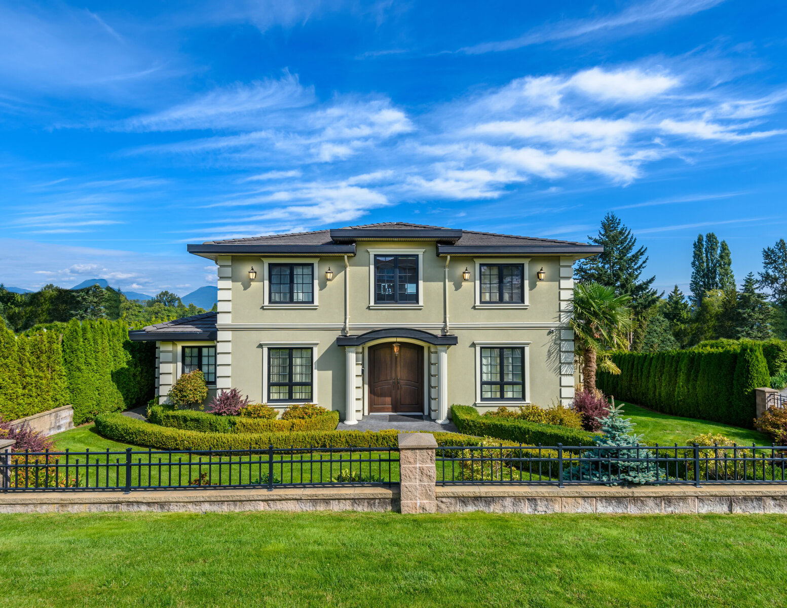 Large two-story house with green lawn, black fence, and blue sky