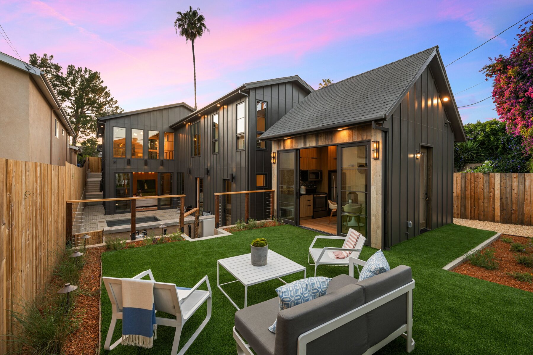 Modern backyard with green lawn, outdoor furniture, and two dark-colored houses