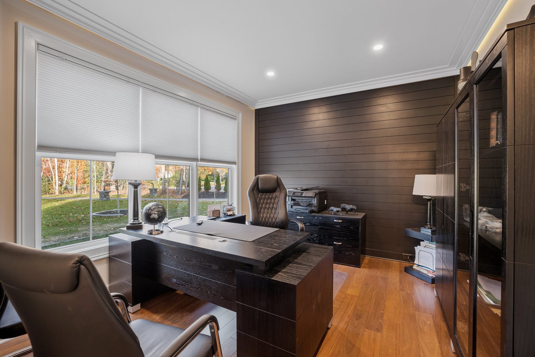Modern home office with dark wood furniture and large window overlooking a yard
