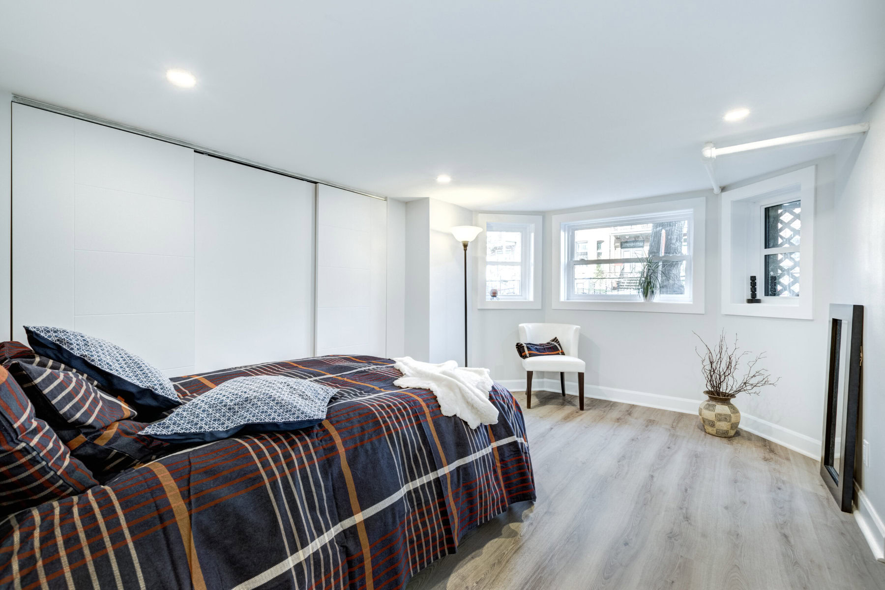 Bedroom with plaid bedding, white walls, and light wood flooring