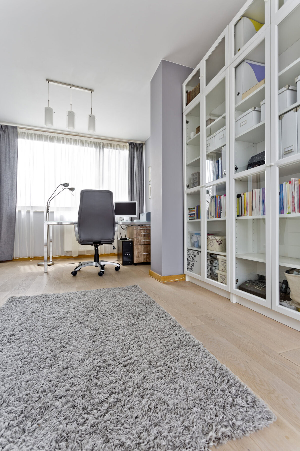 Home office with a desk, chair, computer, and large white bookshelves.