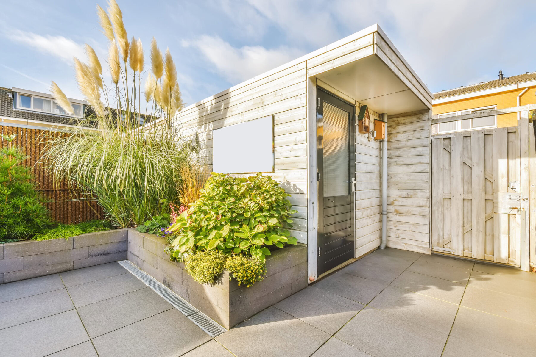 Modern garden shed with pampas grass and various plants under a blue sky