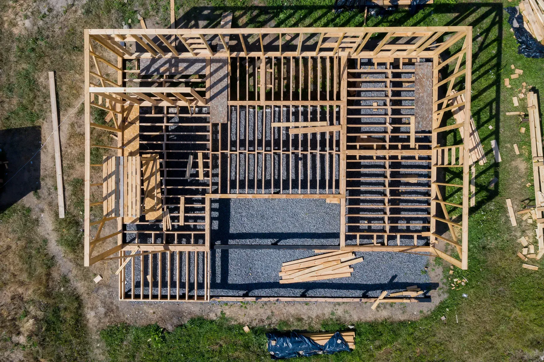 Aerial view of a wooden house frame under construction on a gravel foundation.