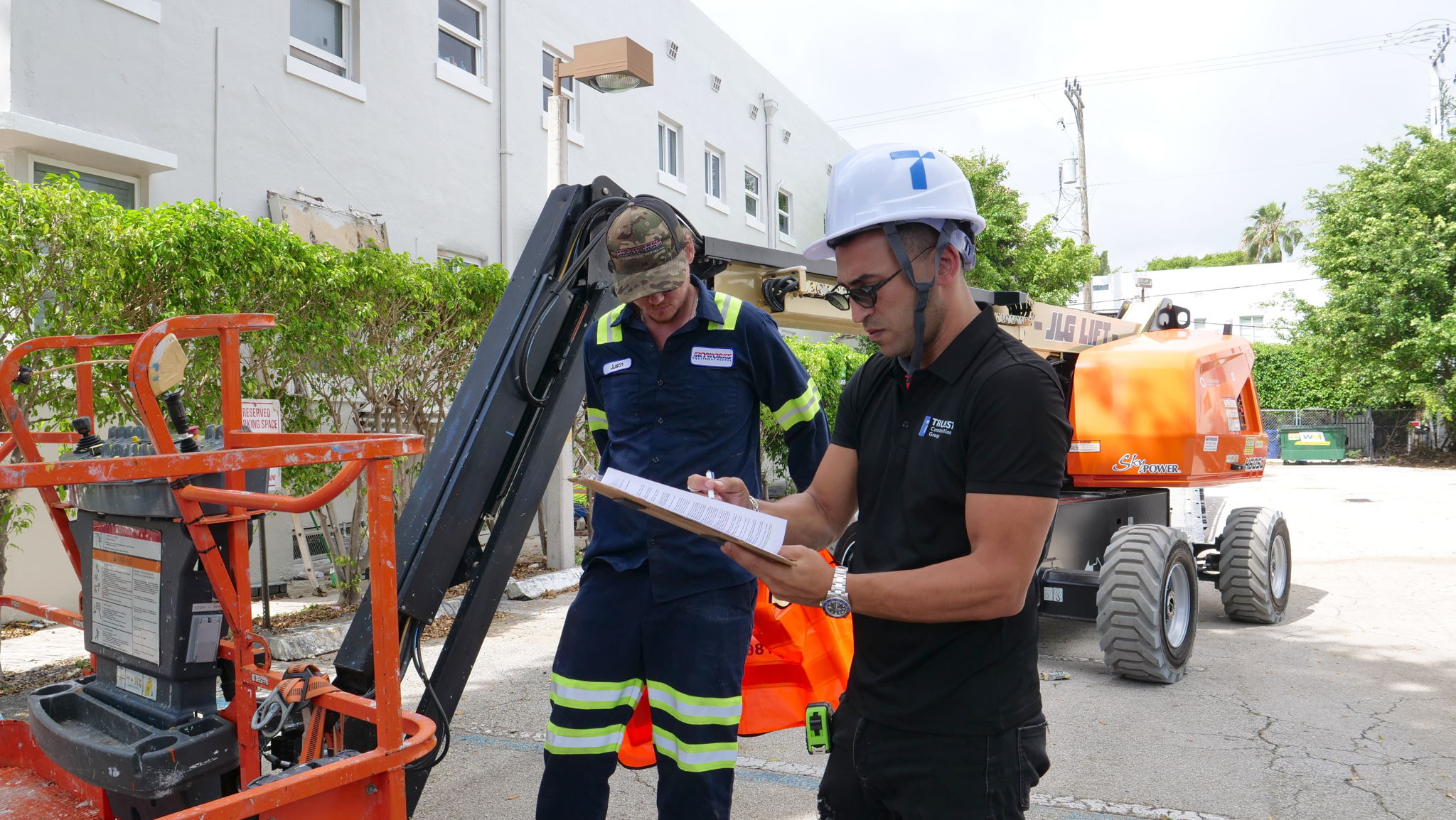 Two men inspecting an orange aerial work platform outdoors