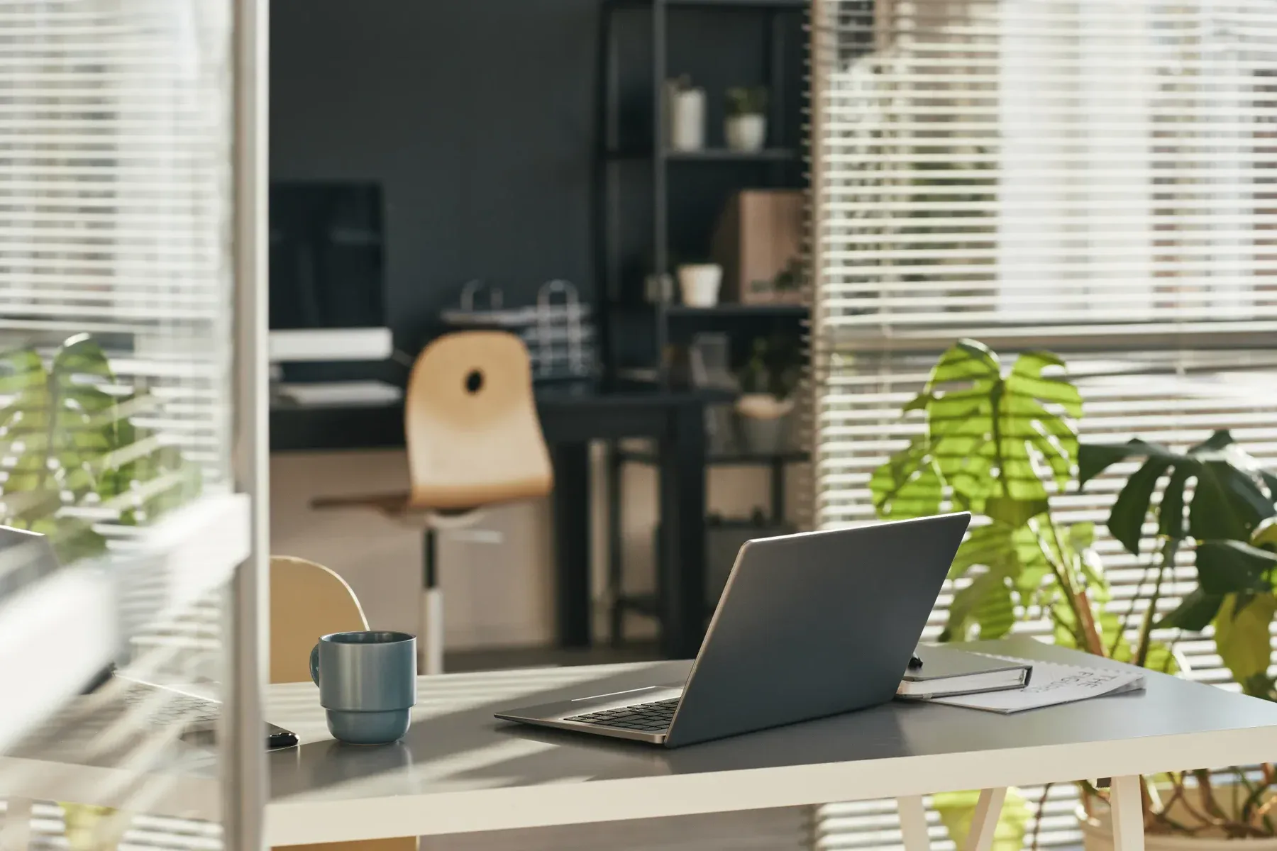 Laptop and mug on a desk in a modern office with blinds.