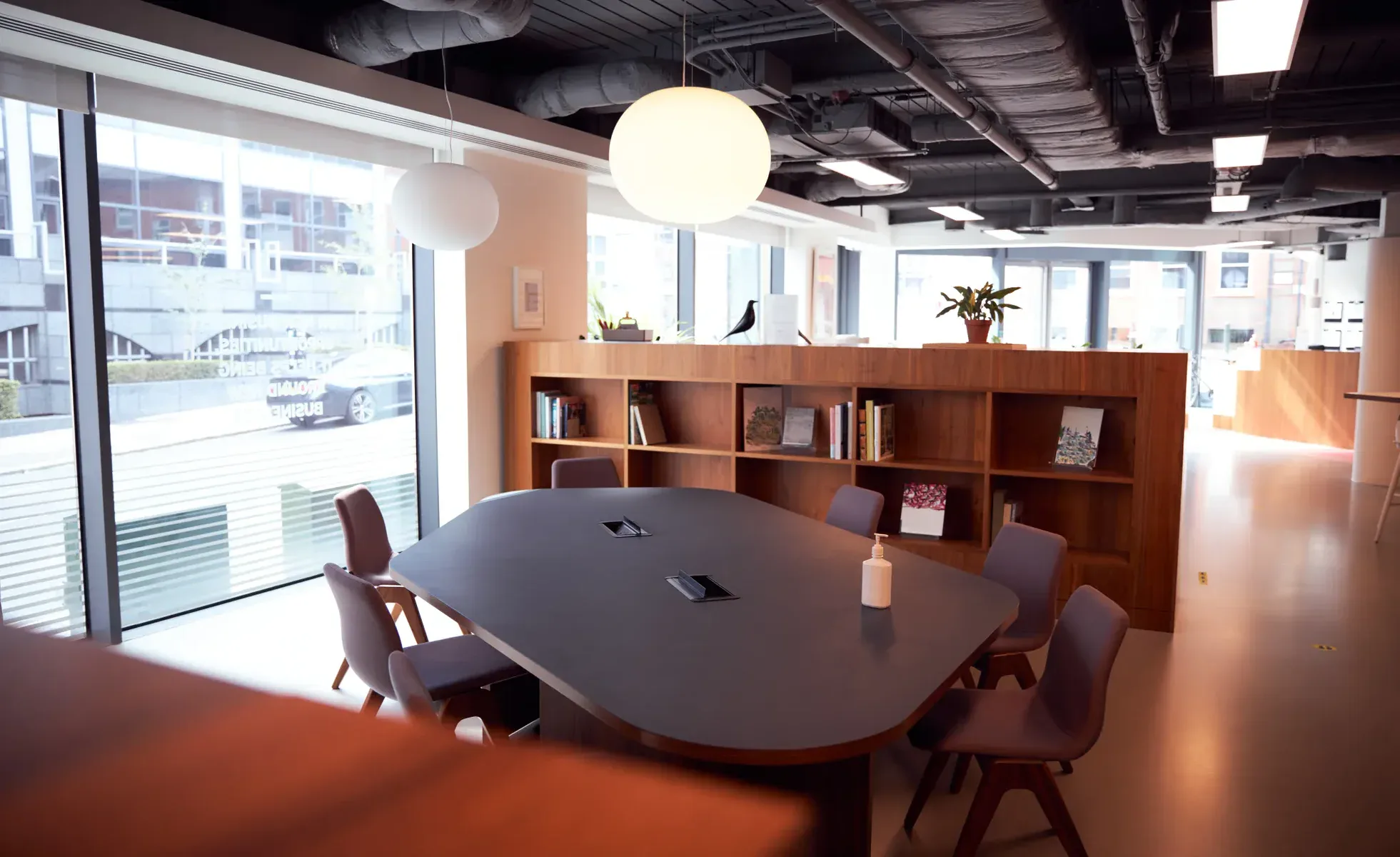 Modern office meeting room with a large table and chairs, and a bookshelf.