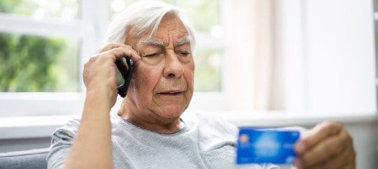 aged man calls on the phone and holds a business card in his hands