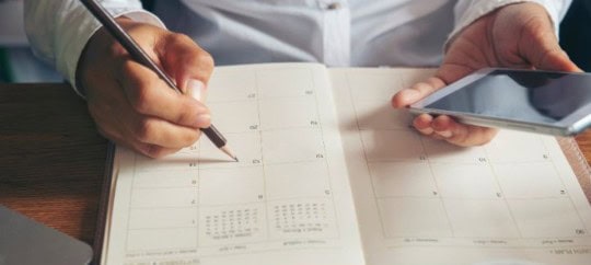 Someone holding phone and setting a target on a calendar in scheduling planner