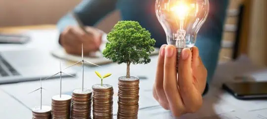 Person holing a lightbulb with growing stacks of coins on table
