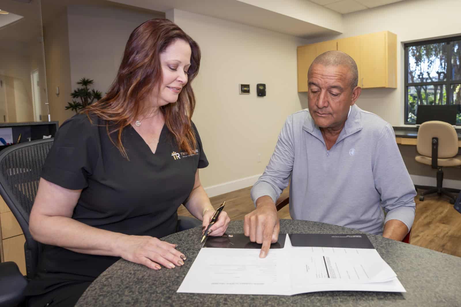 A patient points at paperwork while the dental assistant looks on