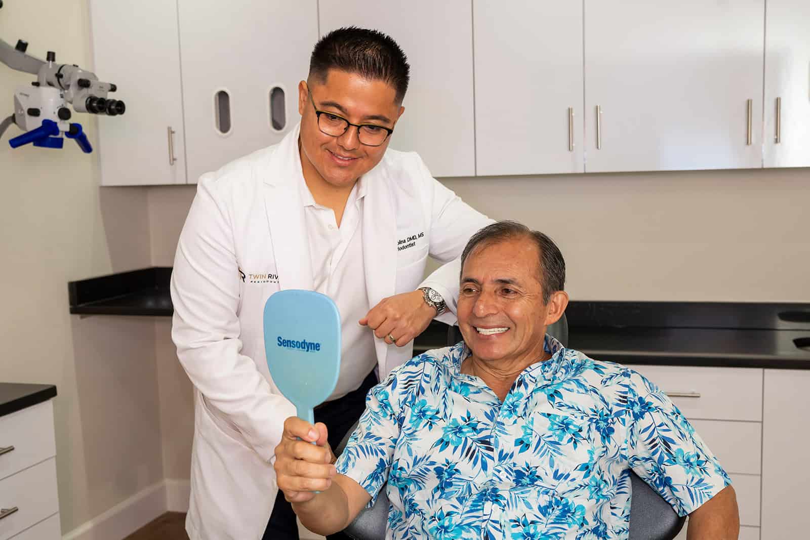 A patient checks his smile while Dr. Molina looks on