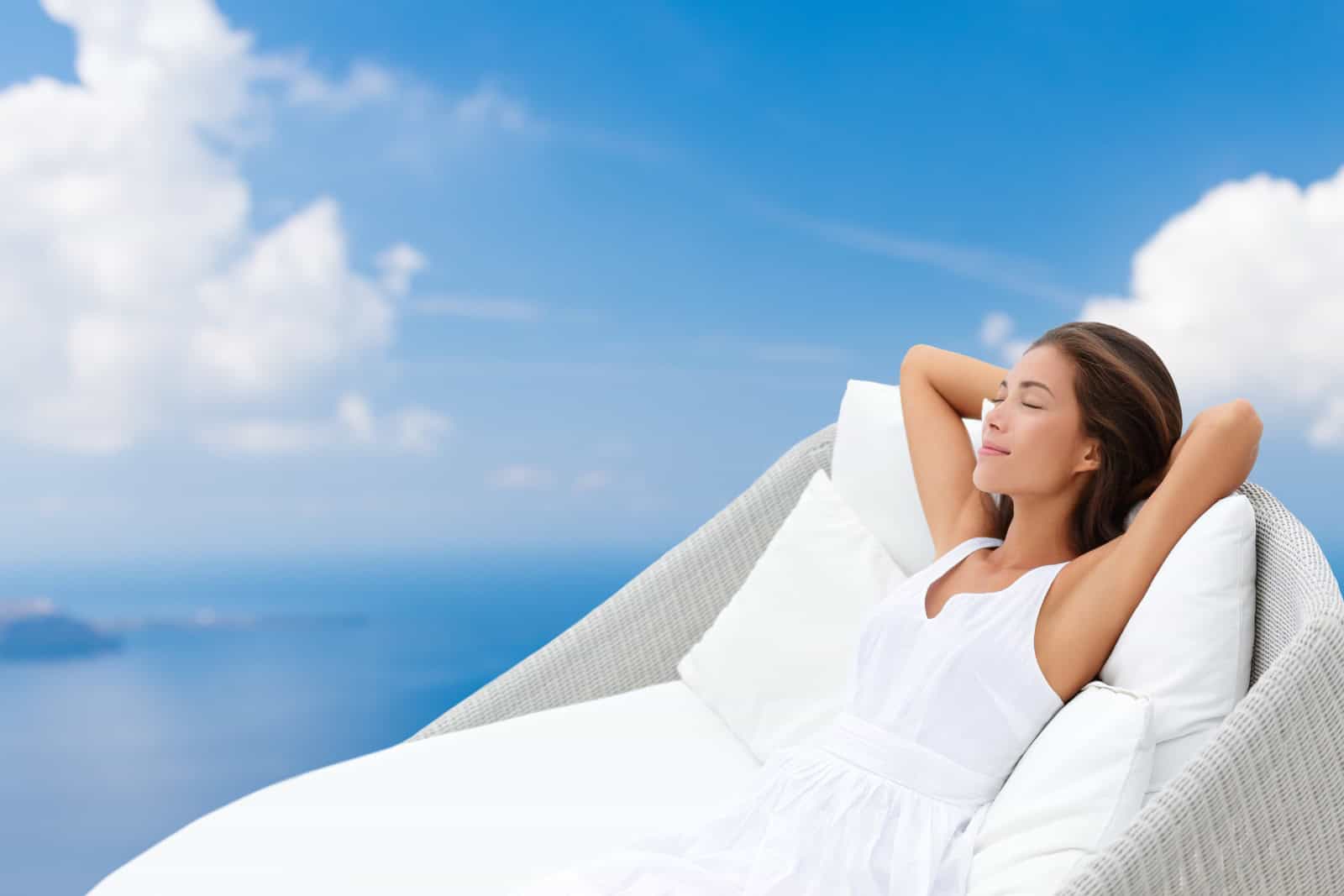 Home lifestyle comfort - woman relaxing sleeping in comfortable sofa chair recliner on blue sky background. Dreaming of wellness, luxury pillows and lounger.