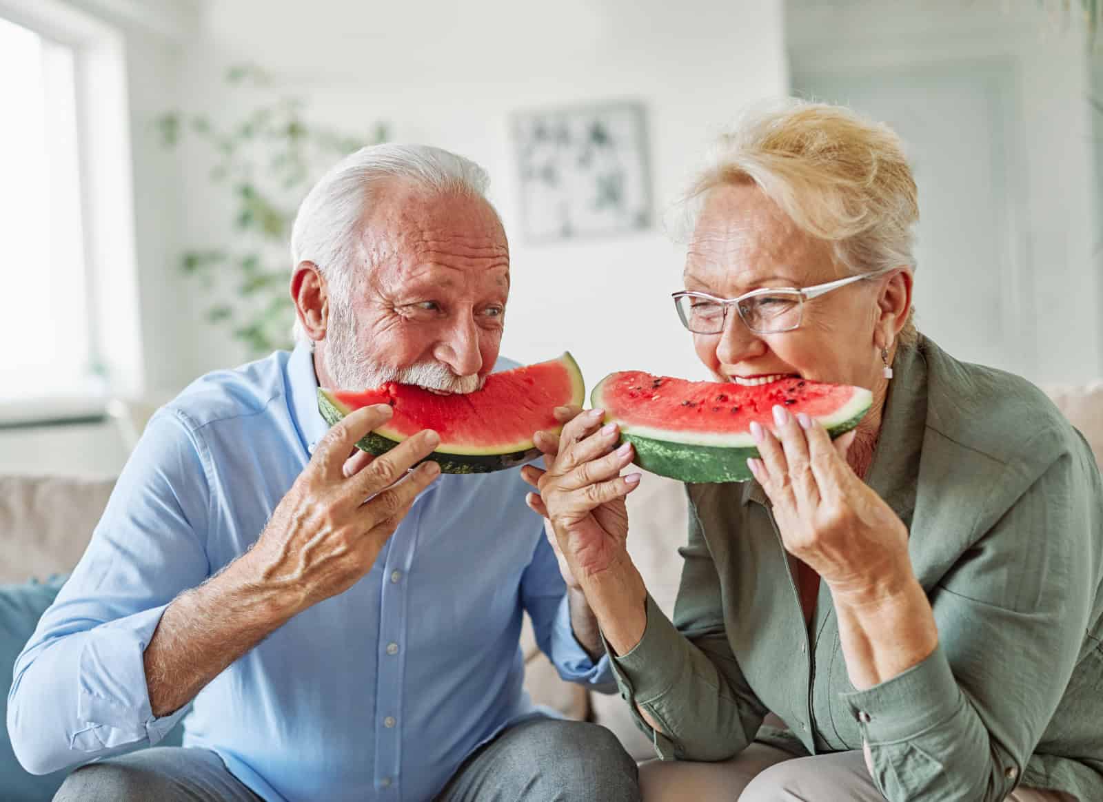 Portrait of a happy senior couple embracing eating watermelon and having fun at home