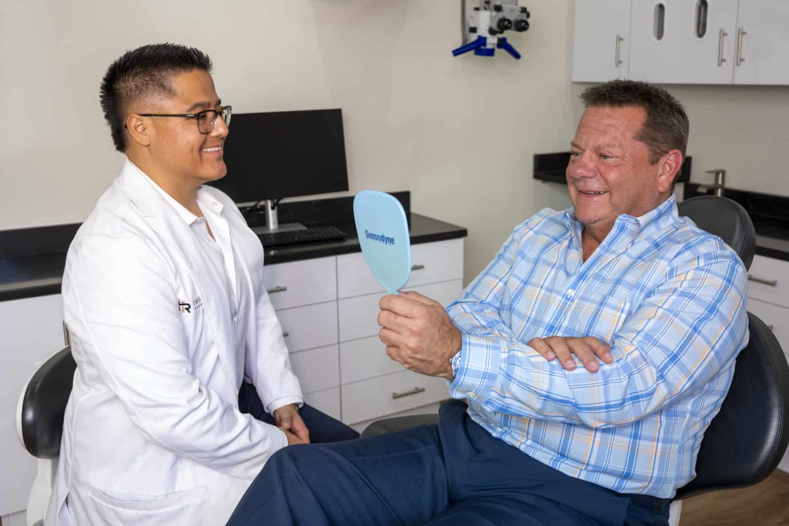 A patient checks his smile while Dr. Molina looks on